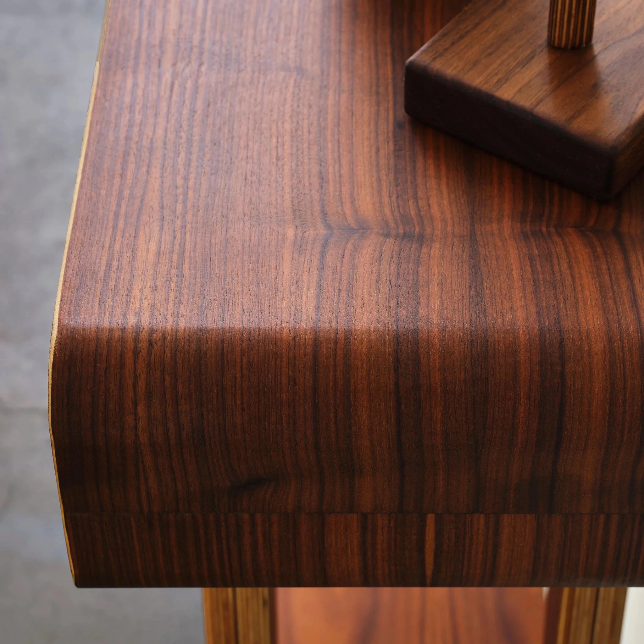 Close-up of walnut entry table's tabletop, showing rich wood grain and curved rounded edge
