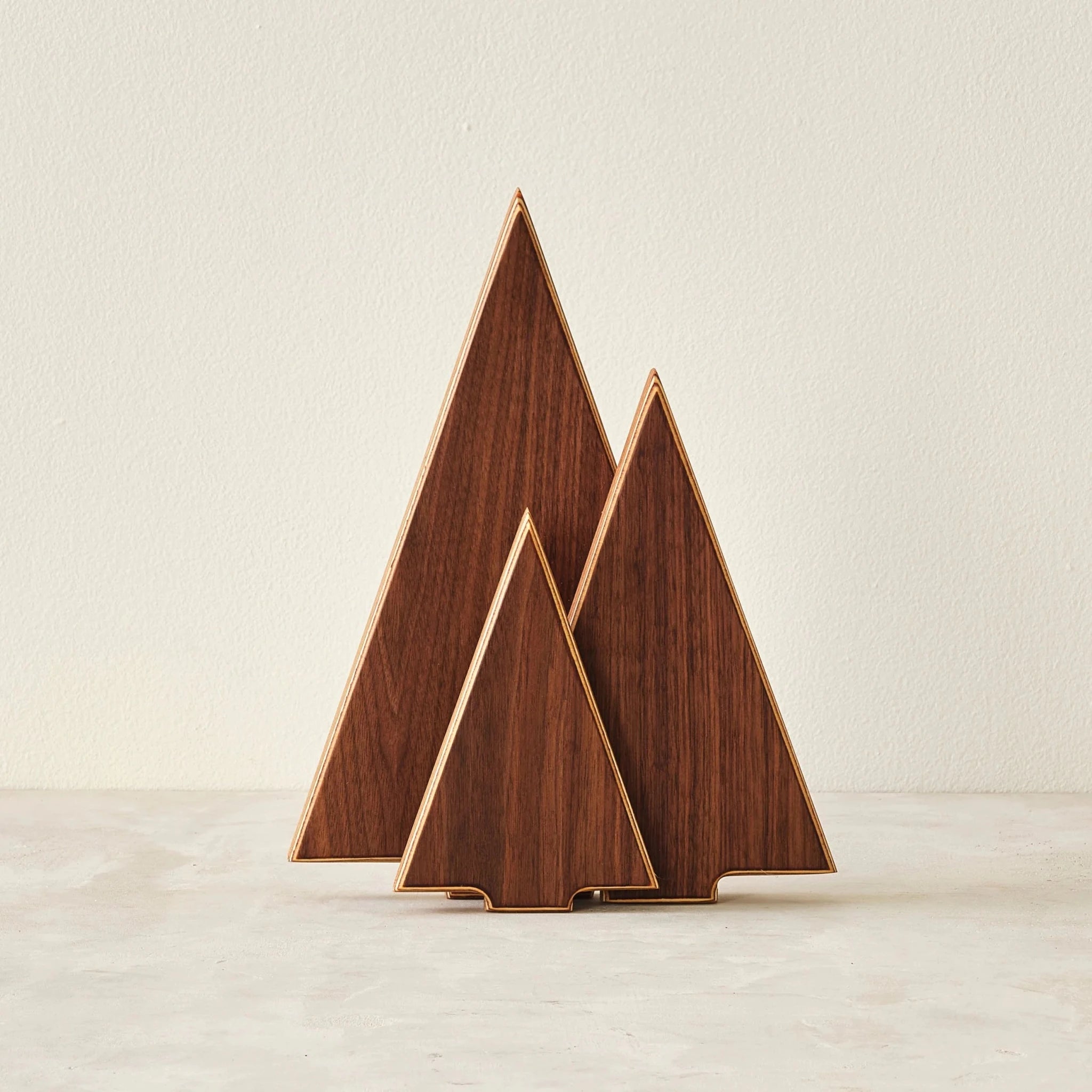 Three walnut triangular tree sculptures with birch edges on light surface