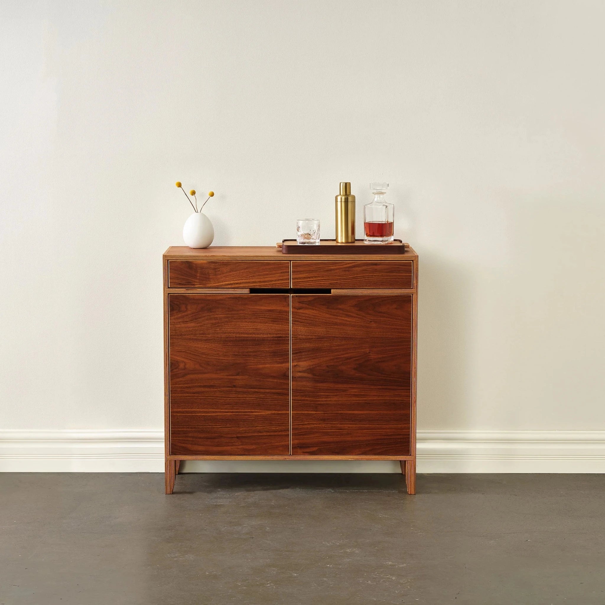 Walnut liquor cabinet front view, closed doors, white vase and barware on top