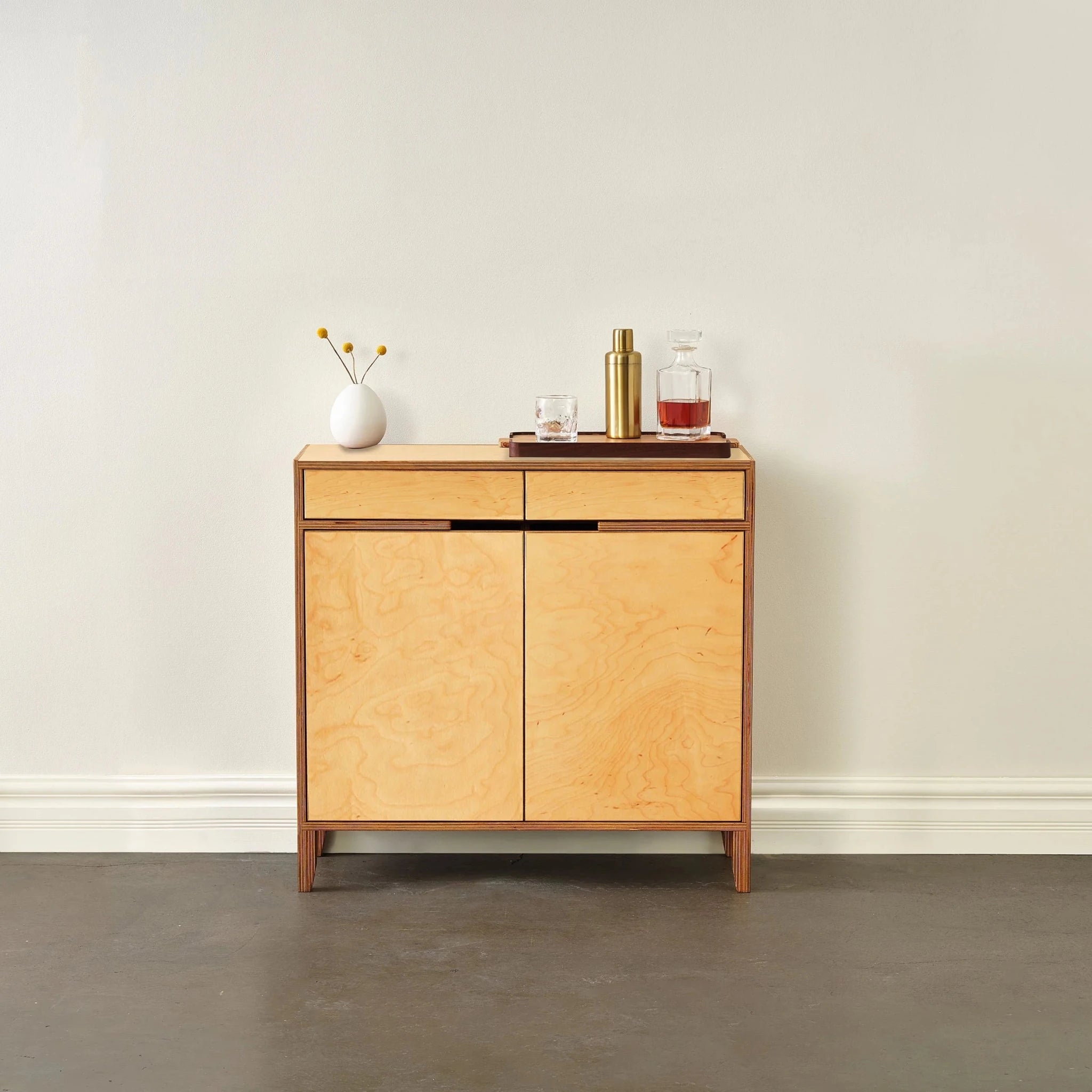 Light maple liquor cabinet, closed doors, styled with vase and barware on top