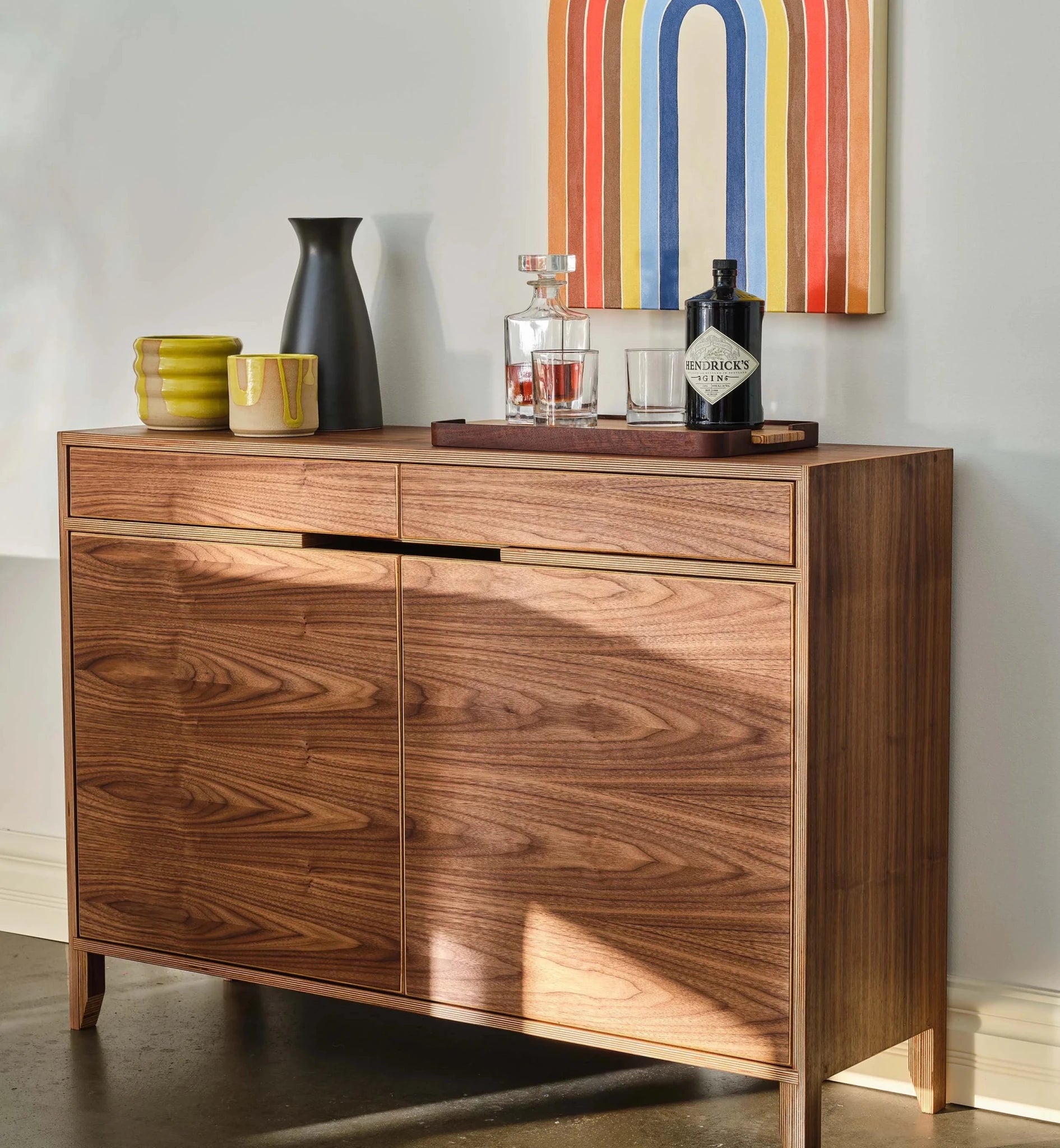 Angled walnut liquor cabinet closeup with ceramic vases, decanter, and gin bottle styled on top