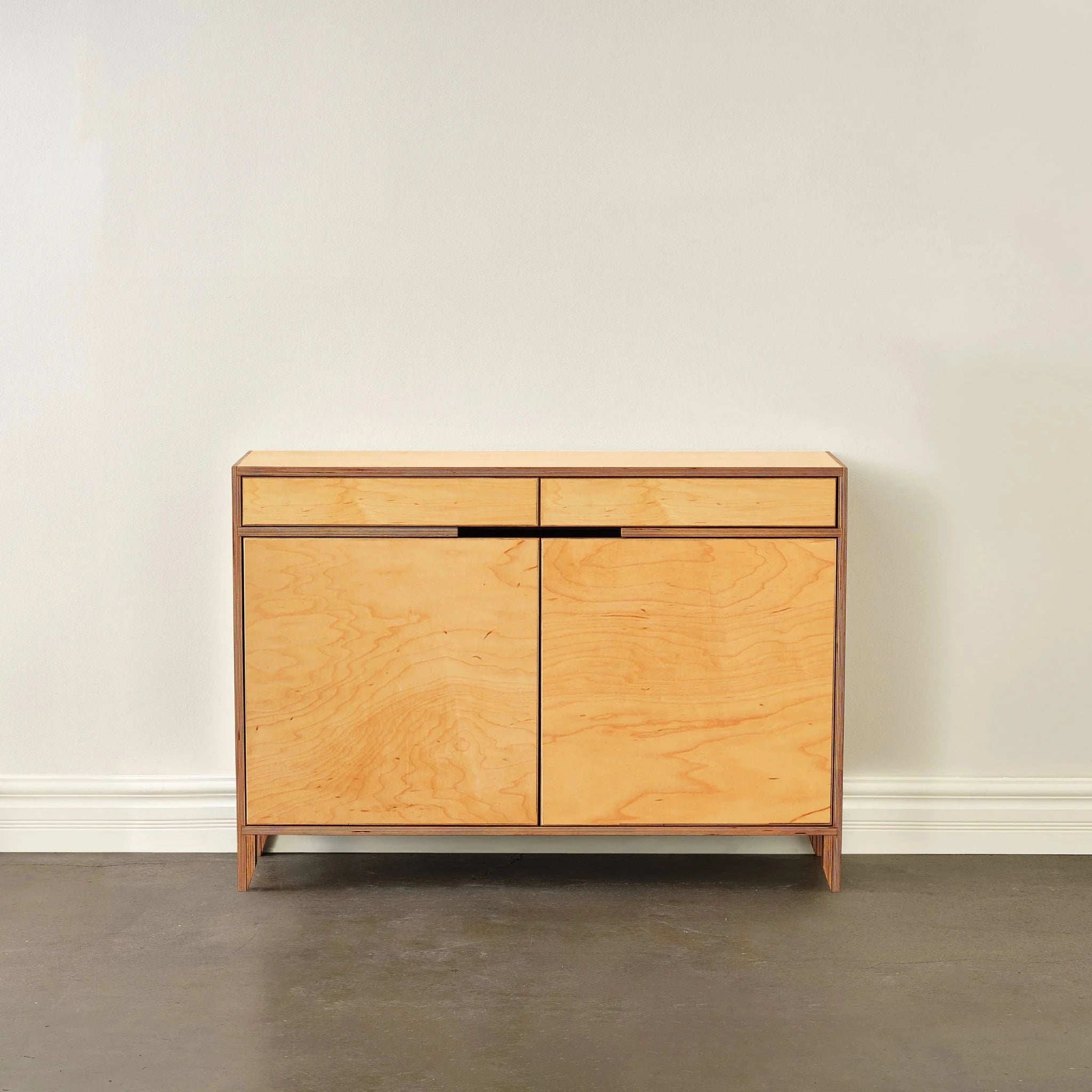 Wide maple liquor cabinet, front view, closed doors against white wall