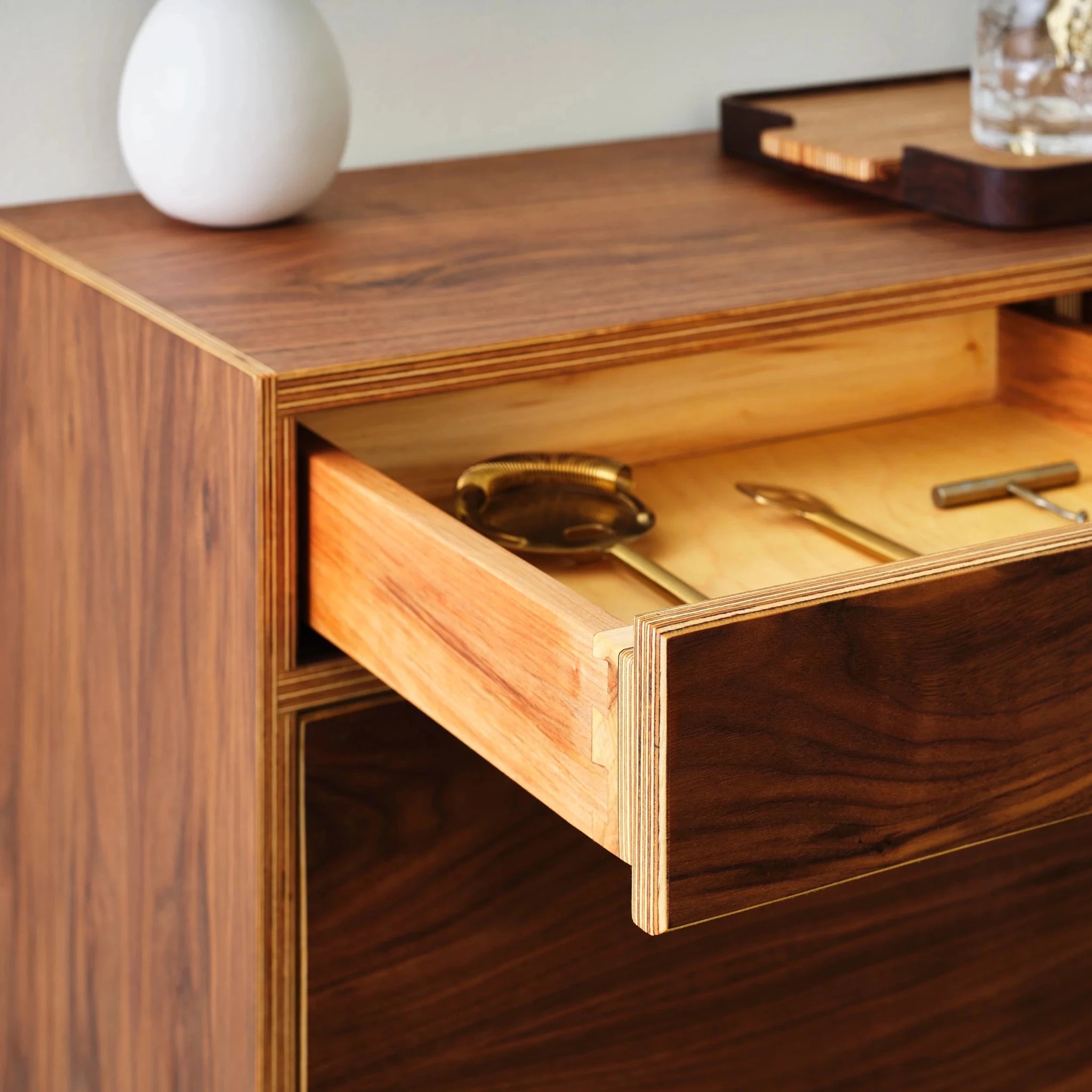 Open walnut drawer revealing brass bar tools inside light maple-lined interior