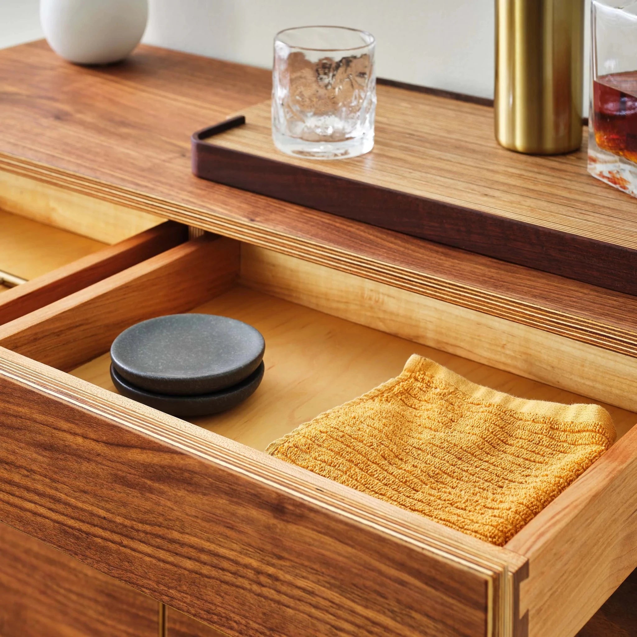 Open drawer holding black stone coasters and folded mustard towel