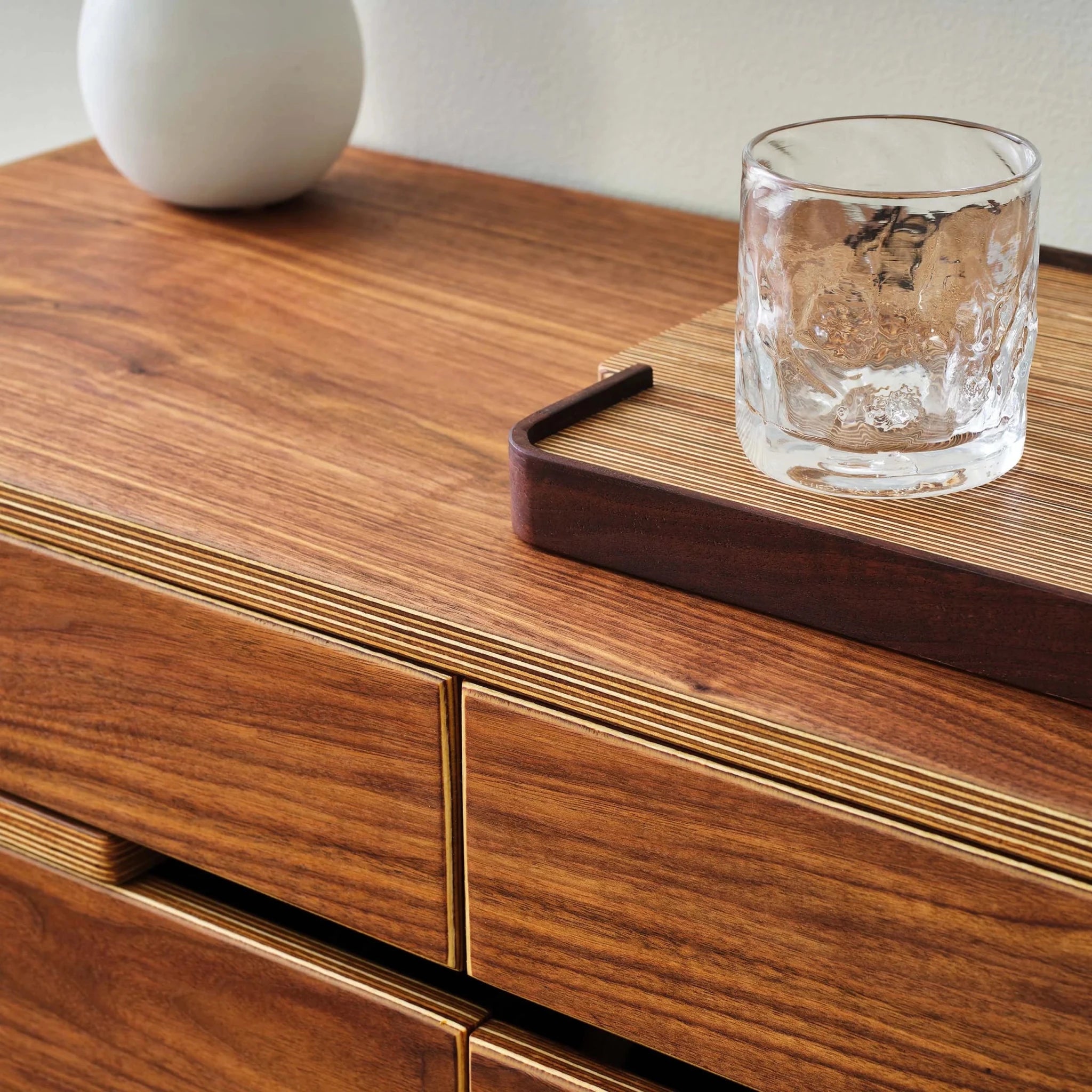 Walnut cabinet top detail with whiskey glass on wood tray and vase