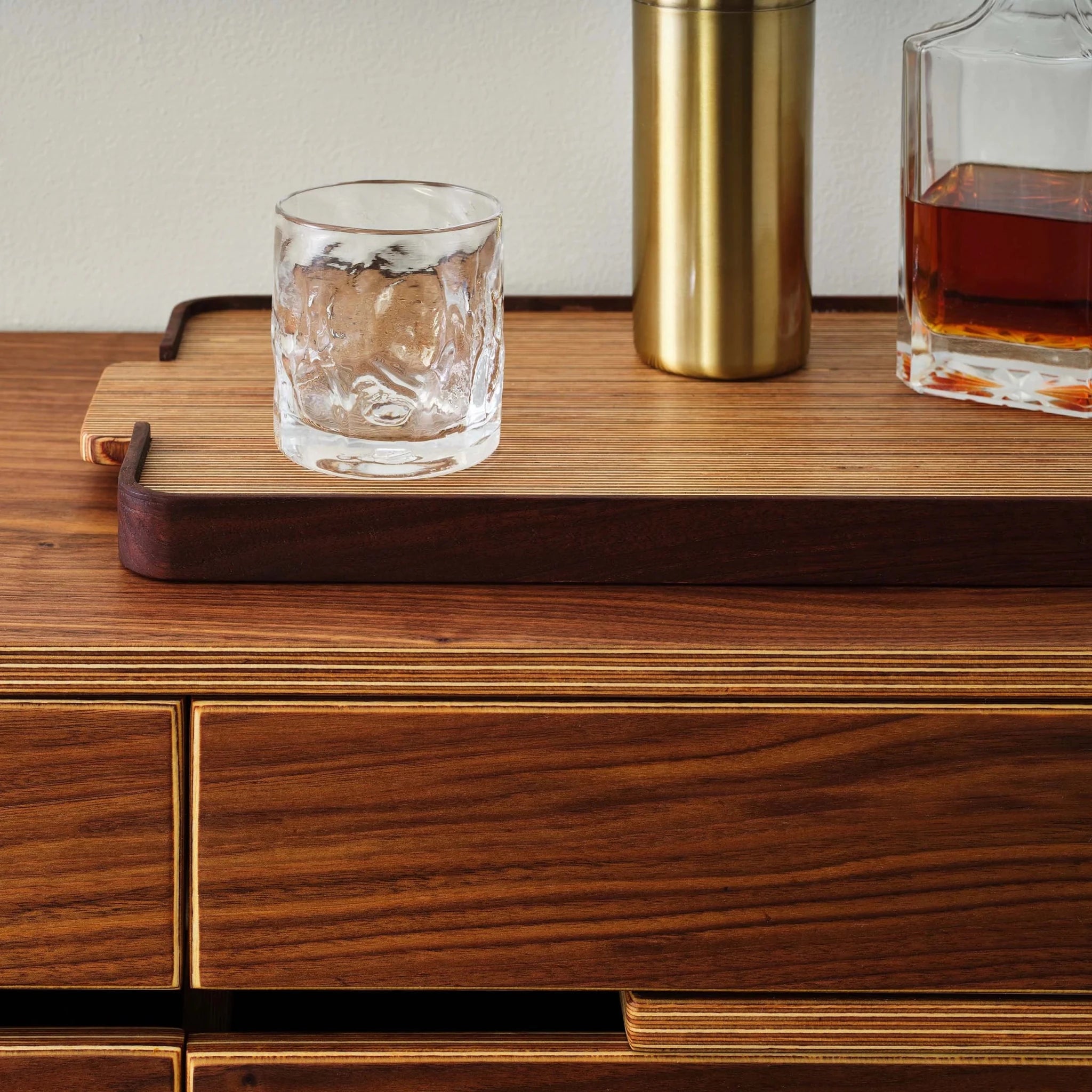 Closeup of cabinet top corner with whiskey glass, brass shaker, and amber decanter