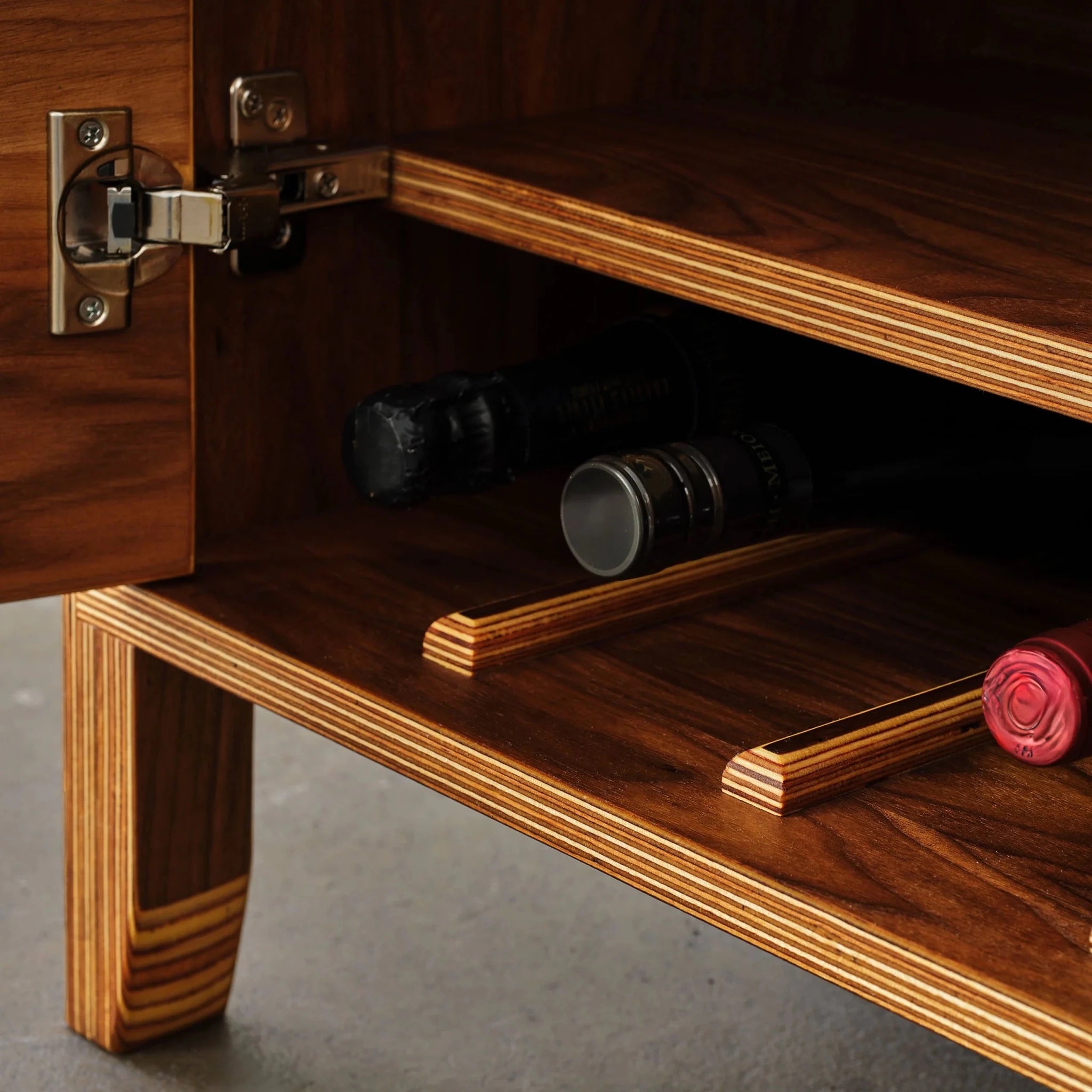 Wine storage detail with bottles resting on birch plywood rails inside cabinet