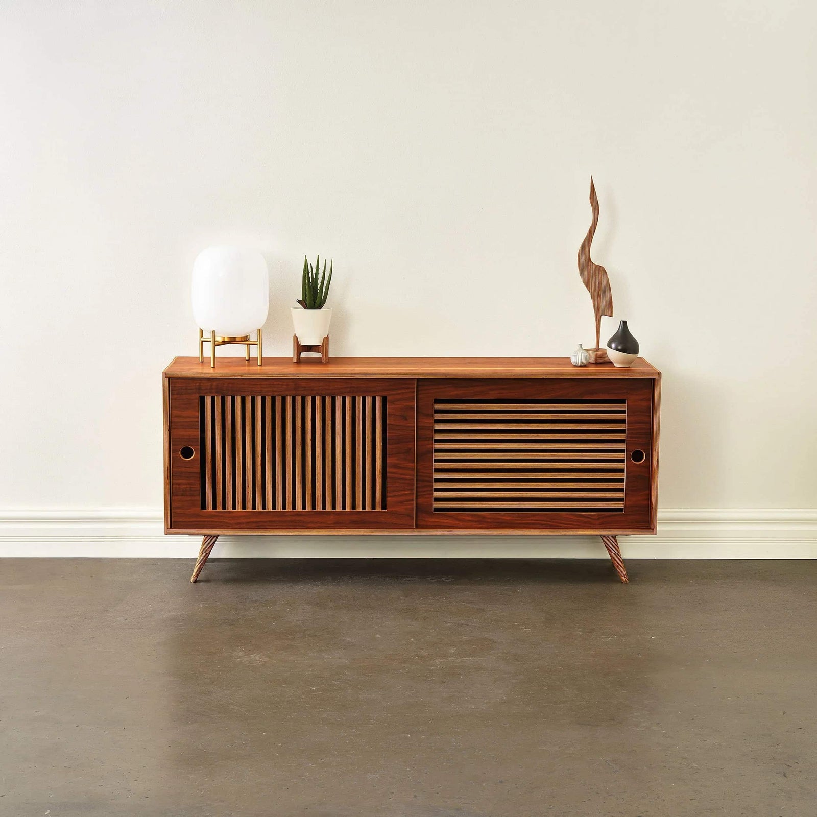 Mid-century modern walnut media console with slatted doors, styled with a globe lamp in a living room