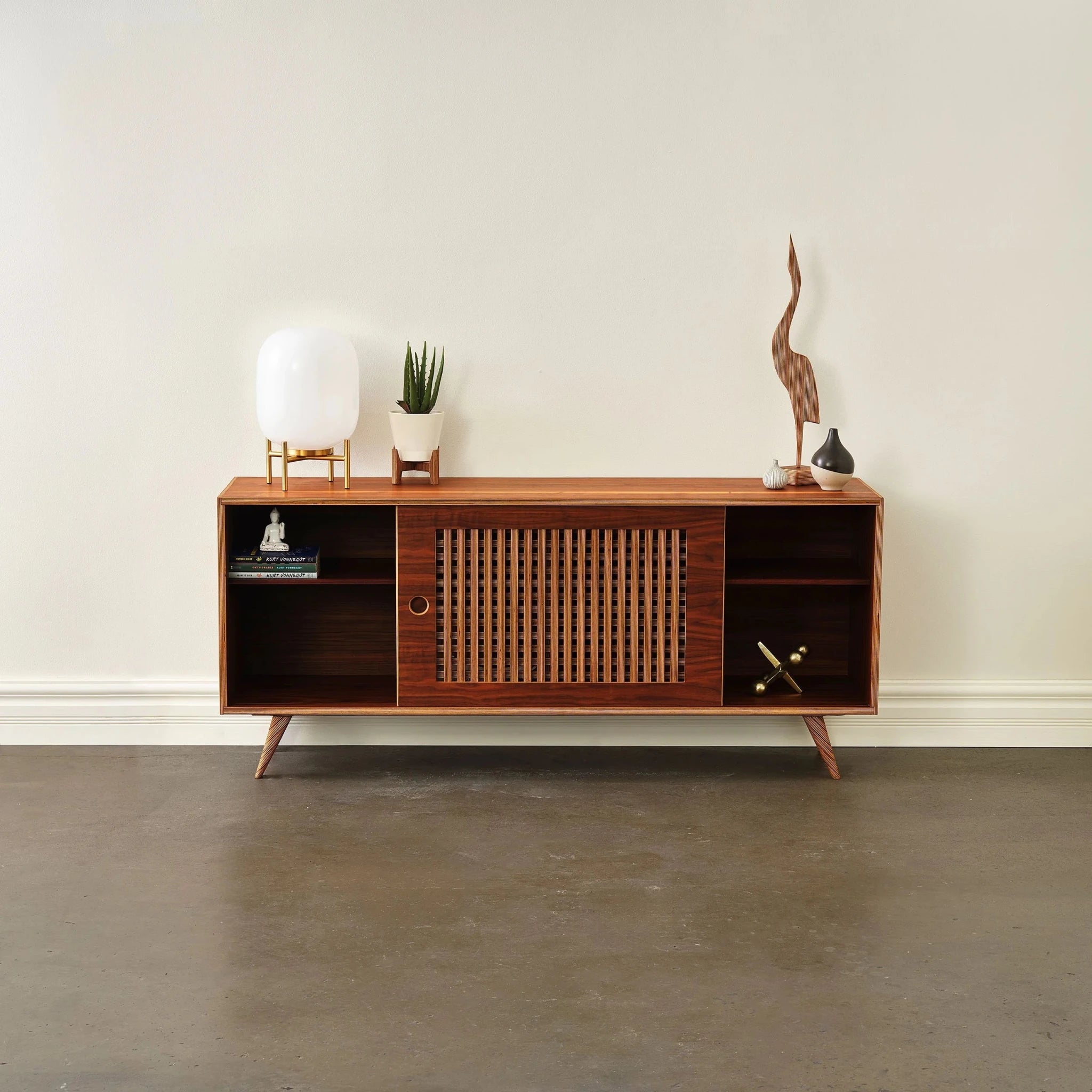 Media console, walnut, sliding slatted door centered, staged with lamp, aloe plant, sculptures