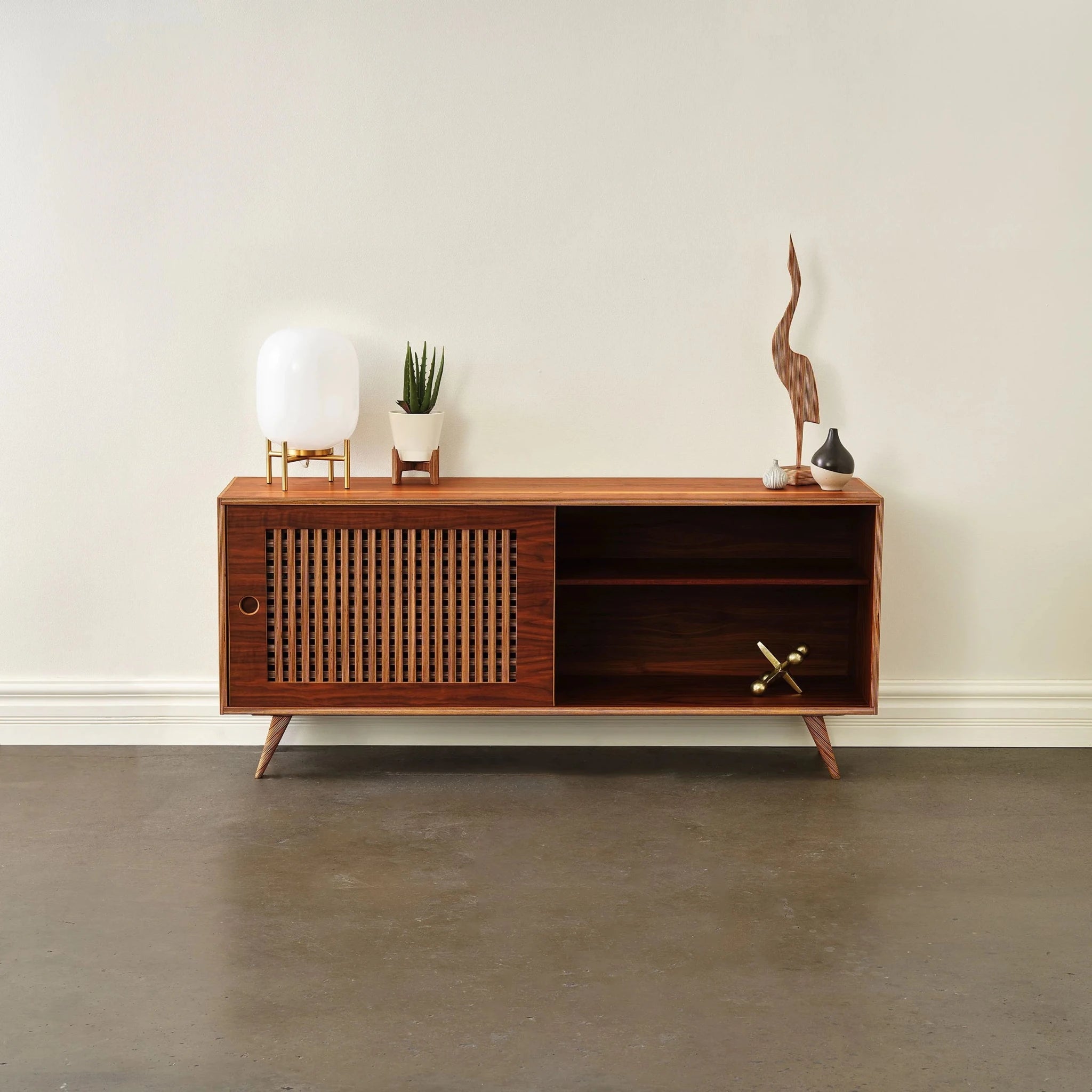 Media console open showing left slatted door, revealing right shelf; lamp and plant on top