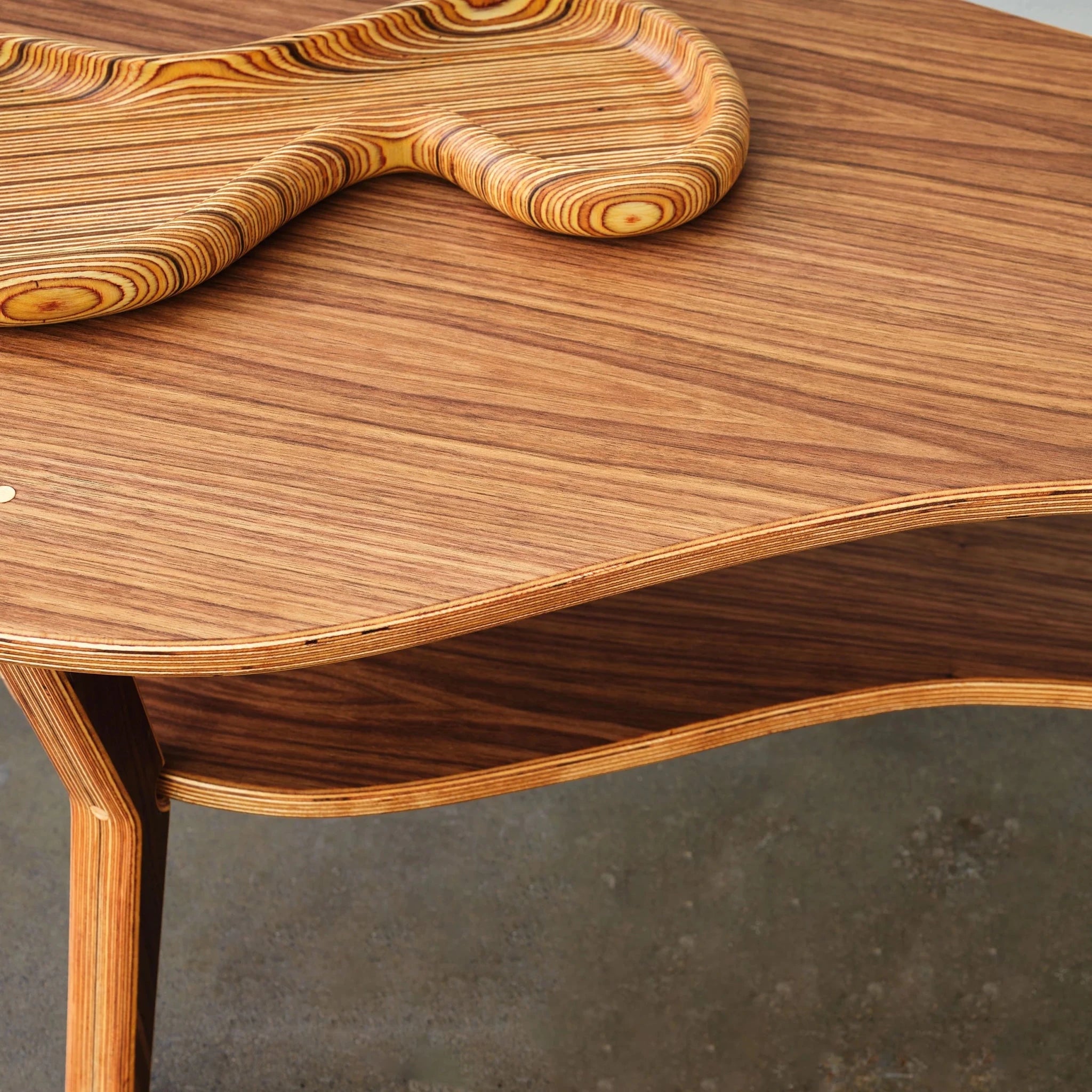 Close-up of walnut cocktail table corner, layered plywood edge, birch tray, concrete floor