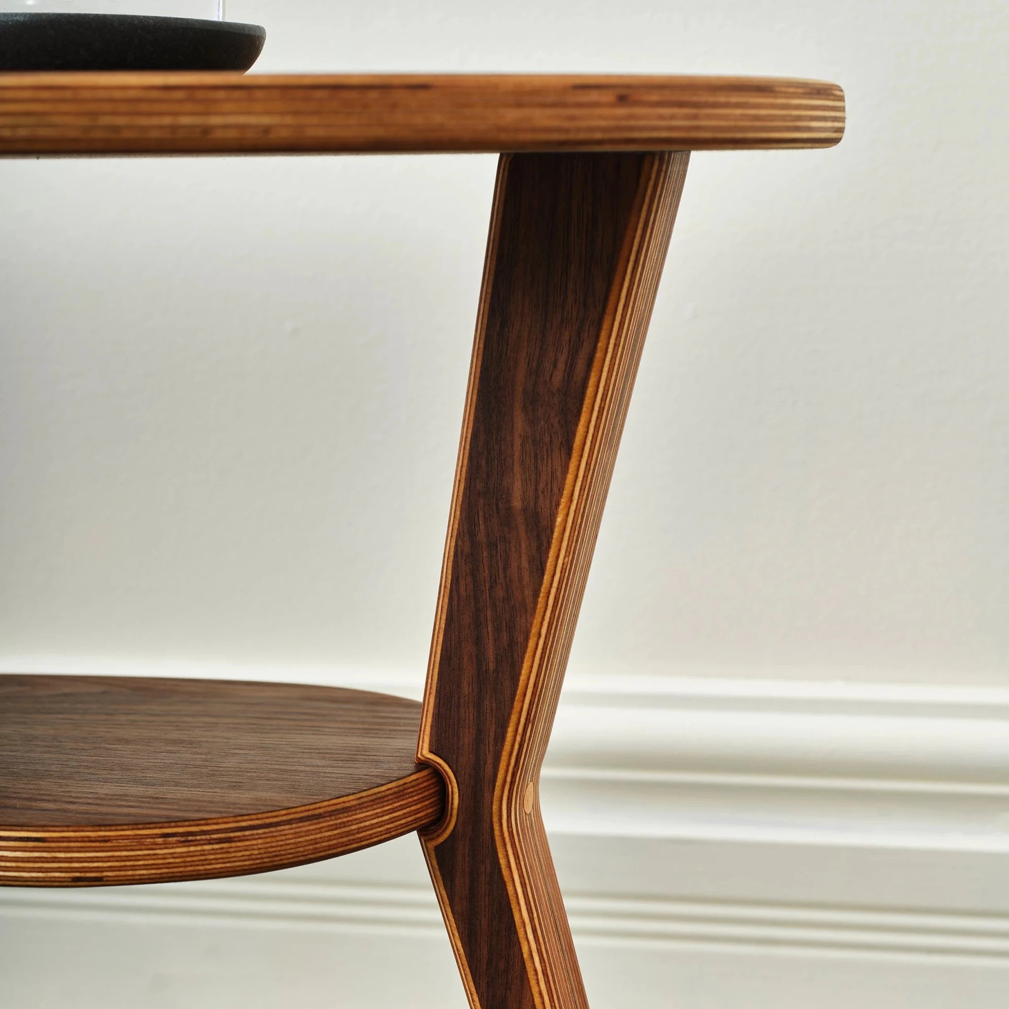 Detail of walnut cocktail table's angled leg and layered-birch plywood edges against white wall