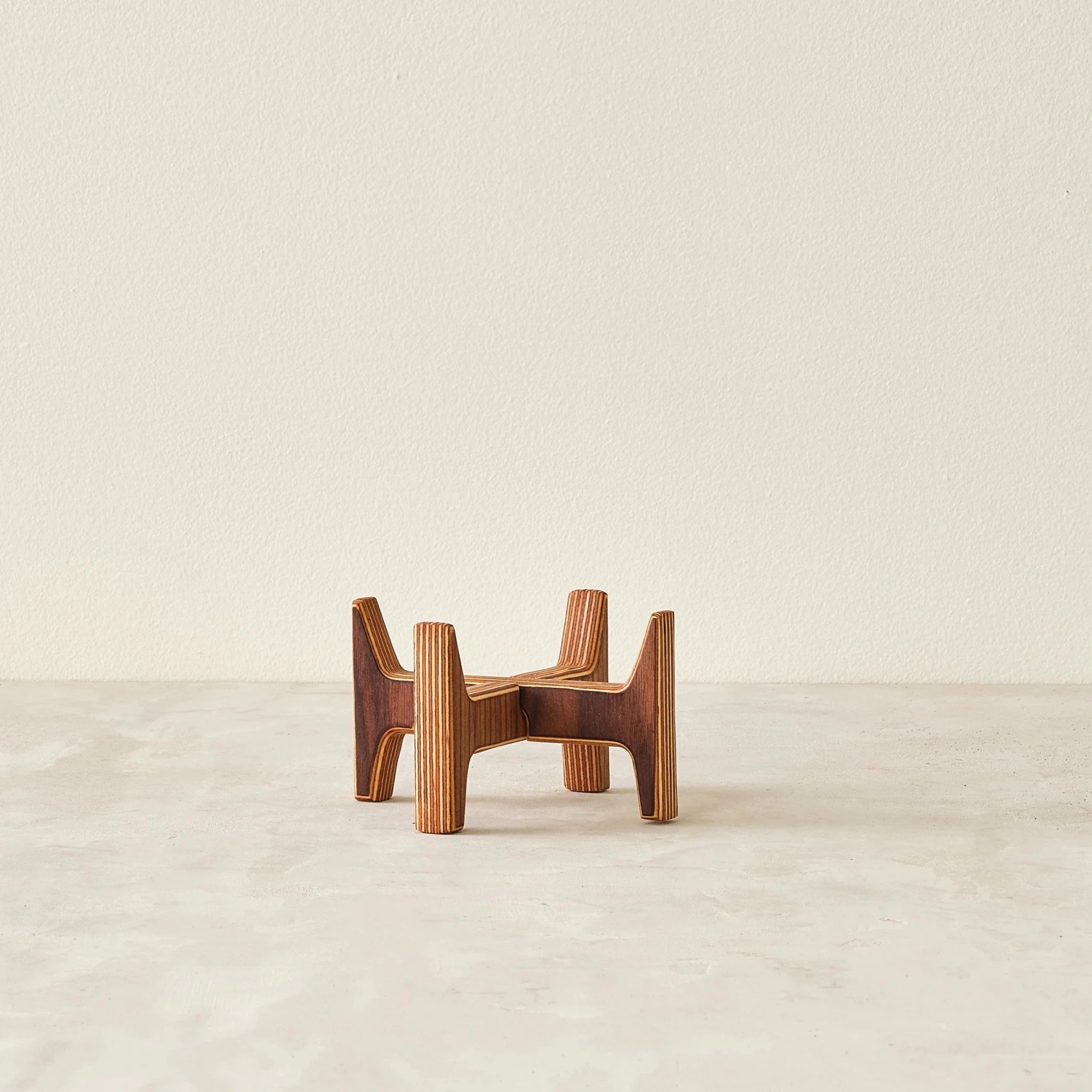Empty small layered birch plywood plant stand, no pot, showing interlocking legs, plain background