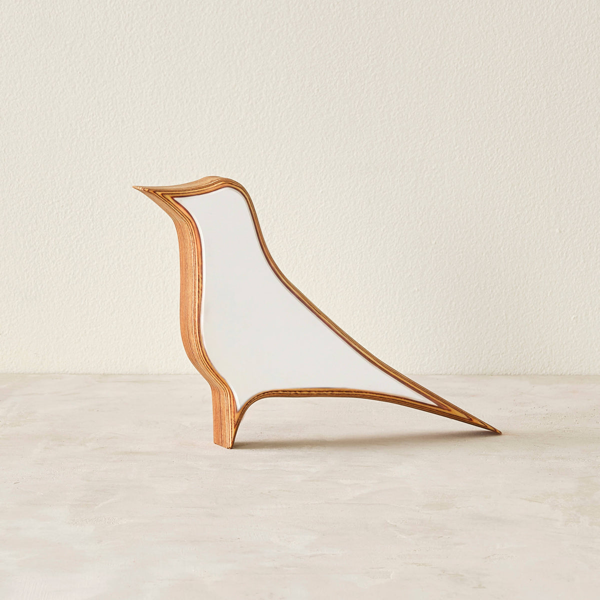 A modern bird-shaped decorative sculpture made of layered wood with a matte white laminate in a neutral space.