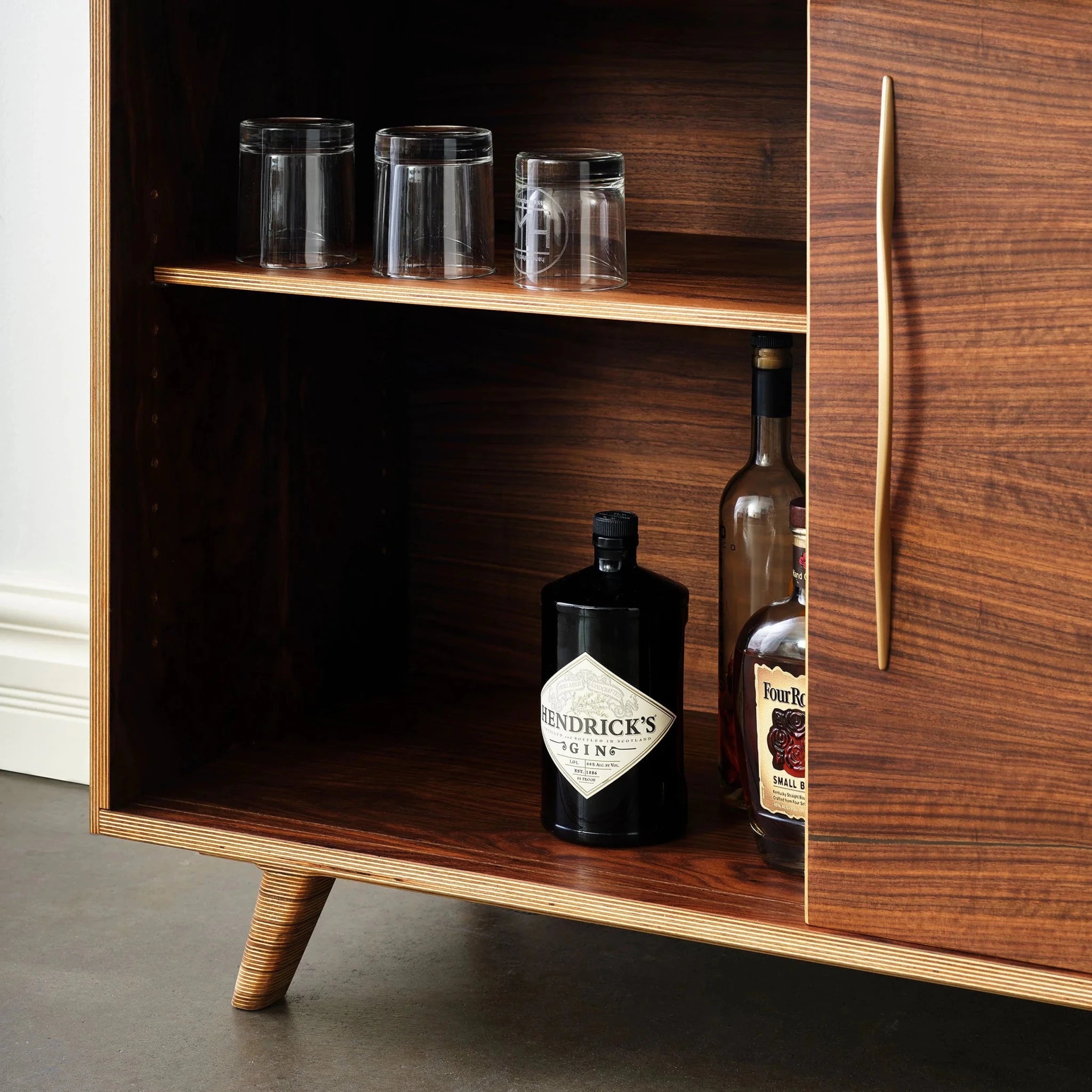 Open walnut cabinet door showing shelved glassware and liquor bottles inside sideboard