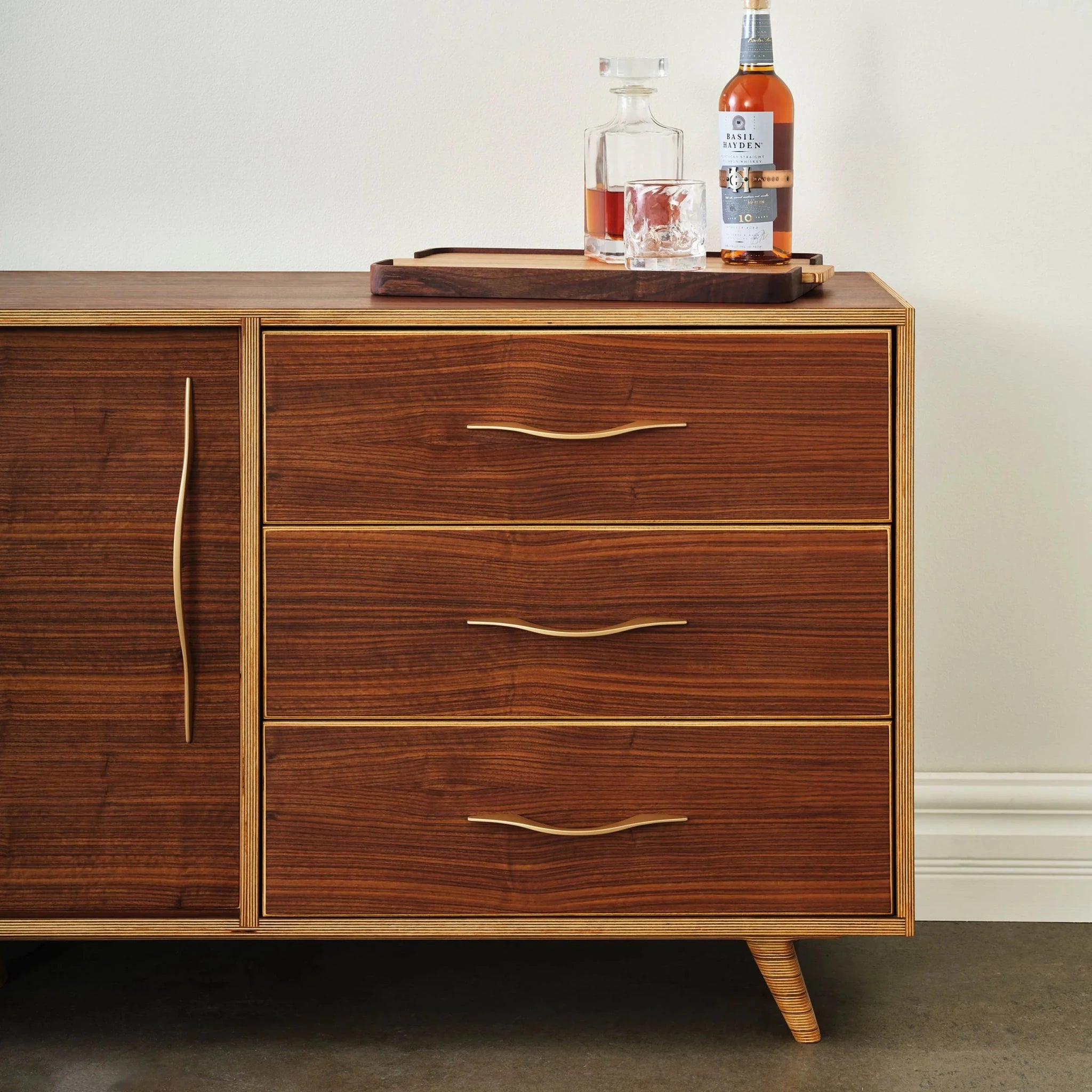 Closeup of walnut sideboard drawers, brass pulls, whiskey decanter and bottle on top