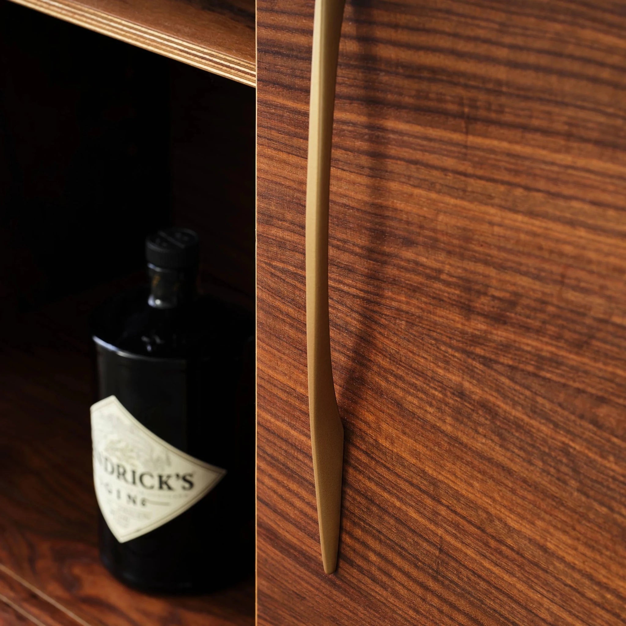 Split view of open cabinet with gin bottle beside walnut door's brass handle