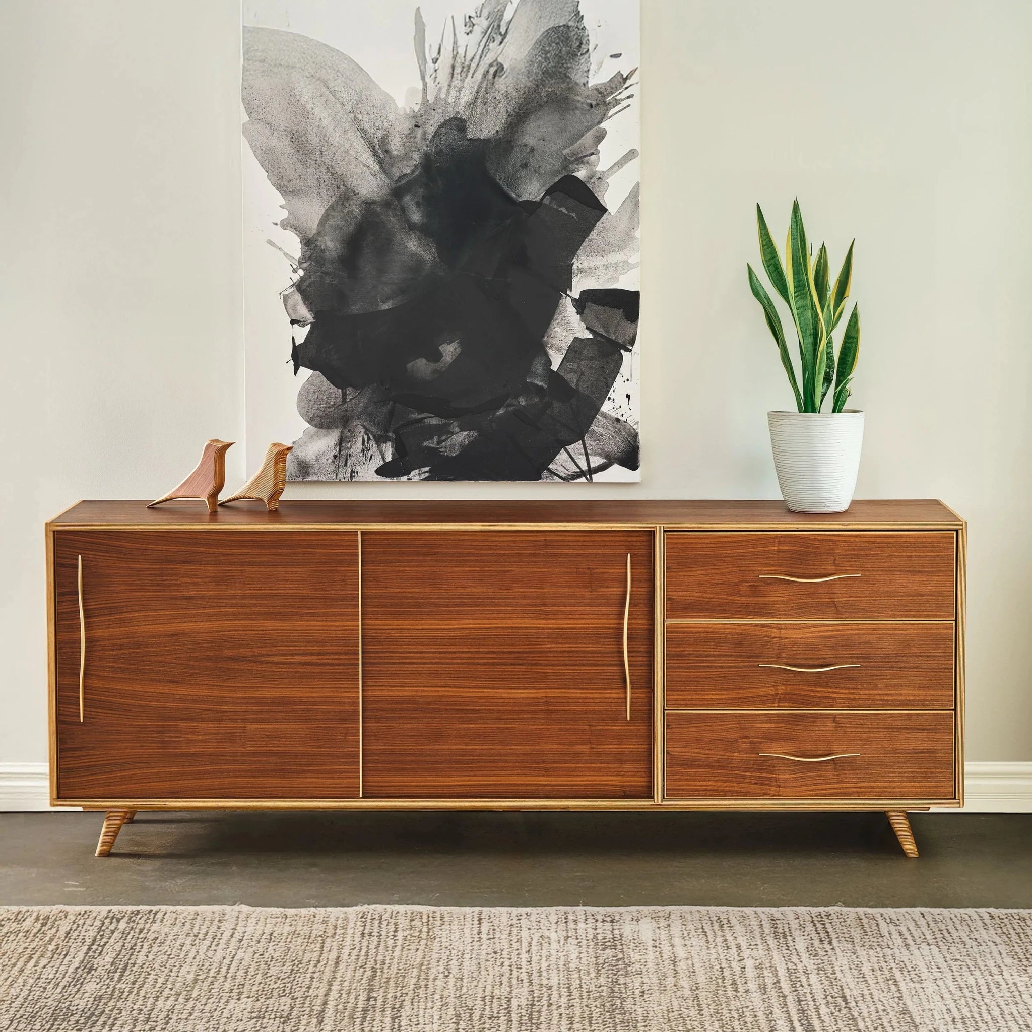 Walnut sideboard with brass handles, closed doors, snake plant and abstract art above
