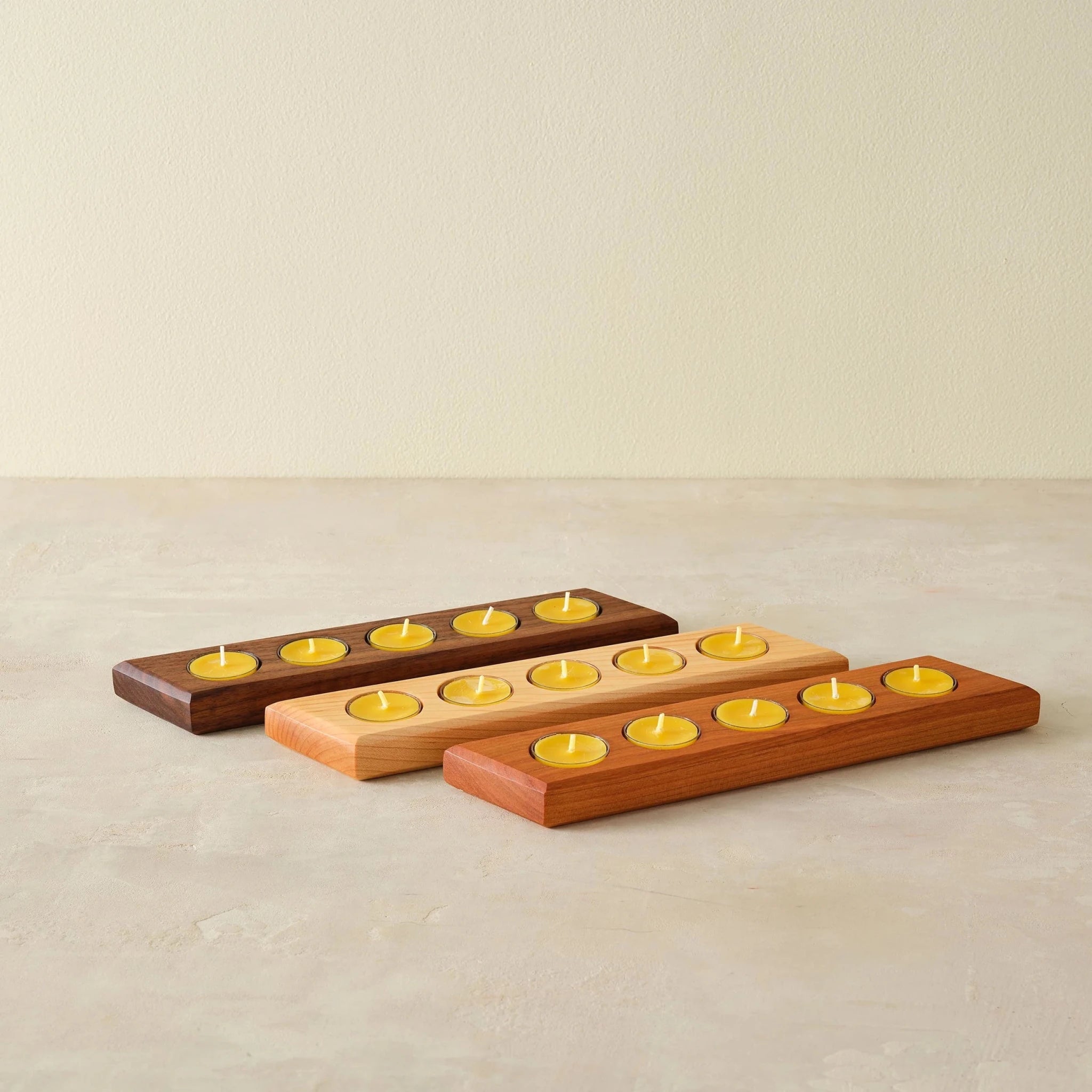 Three tealight bar holders in walnut, maple, cherry, each holding five yellow candles