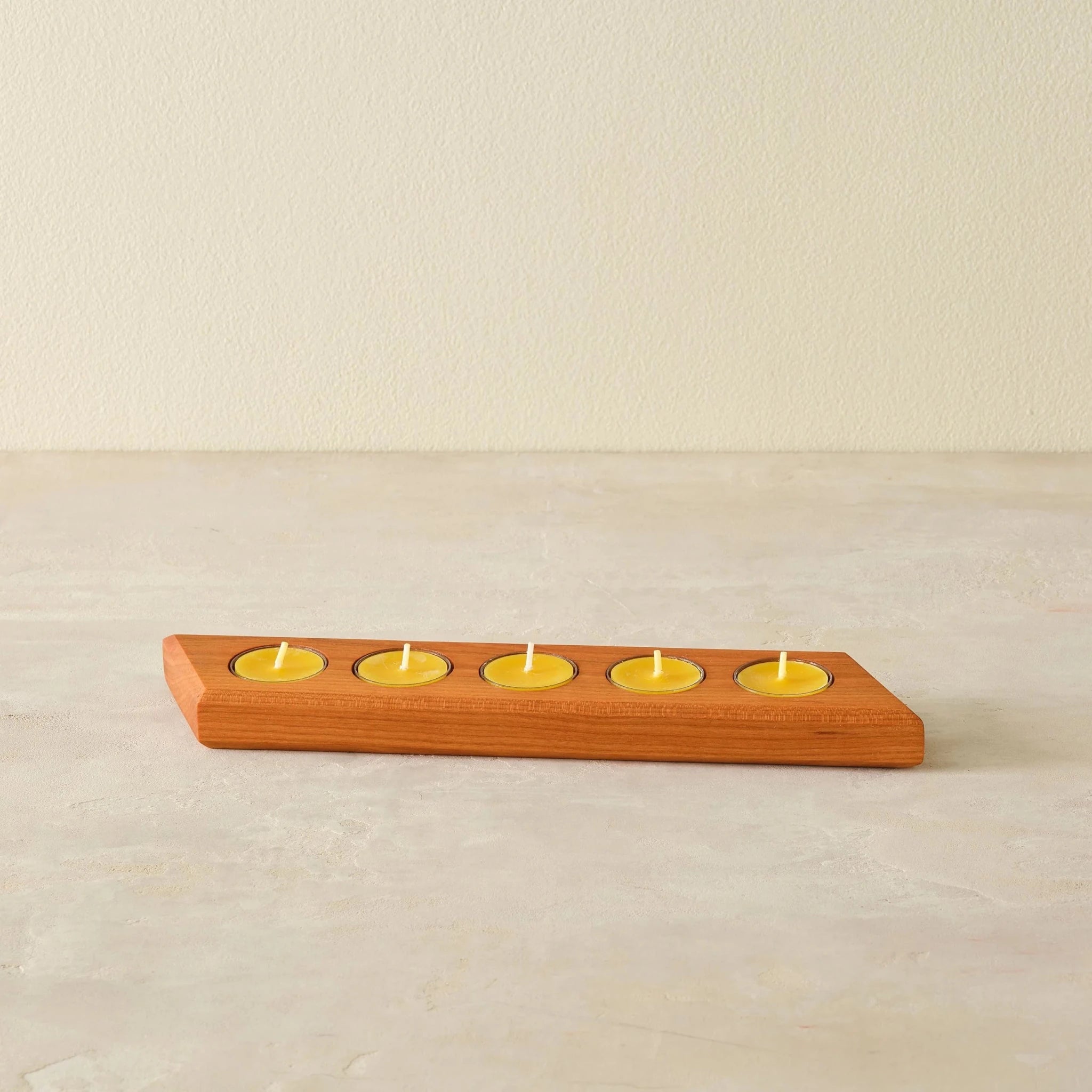 Cherry tealight bar holder with five lit yellow beeswax candles, front angle on neutral surface