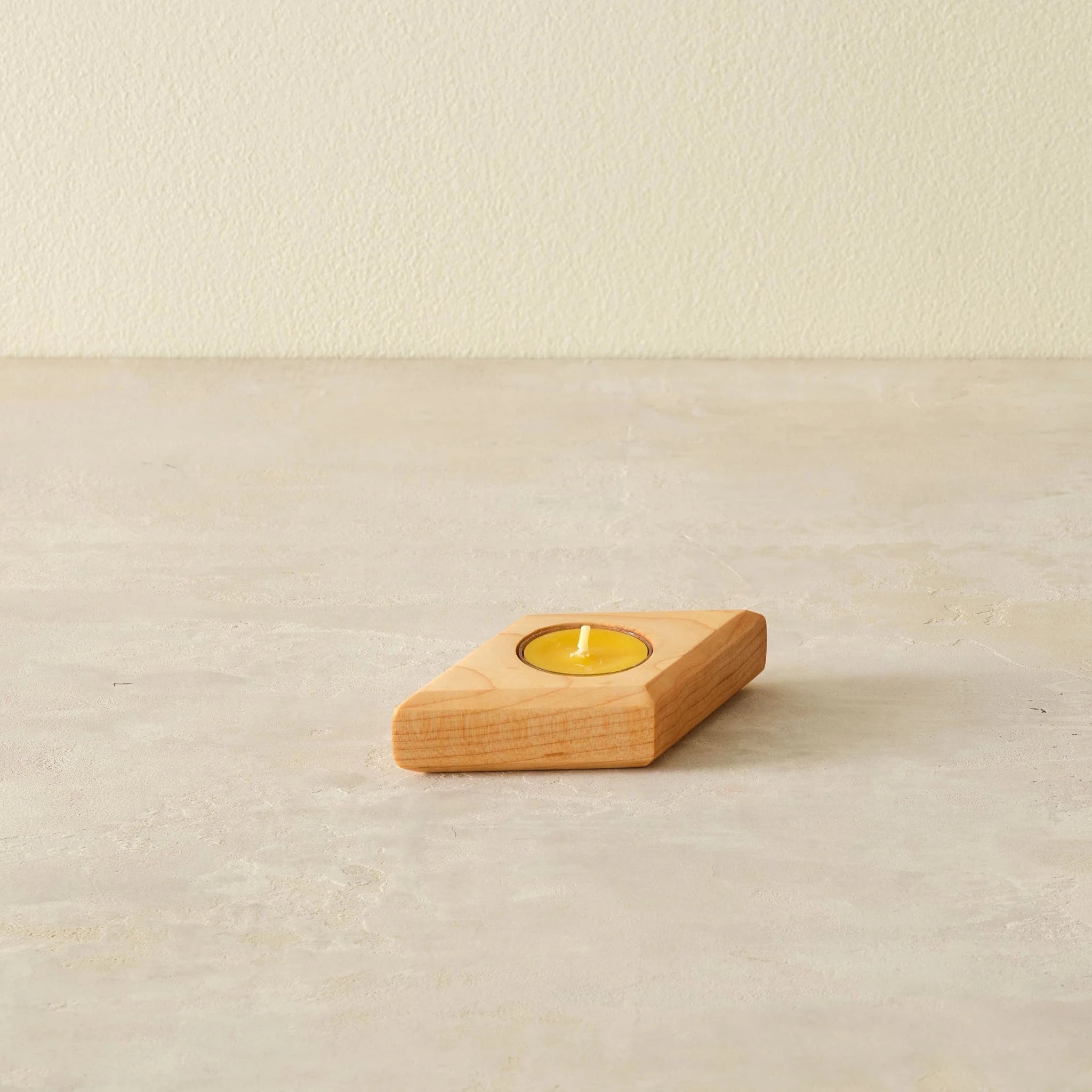 Single maple diamond tealight holder with one yellow beeswax candle, front angle