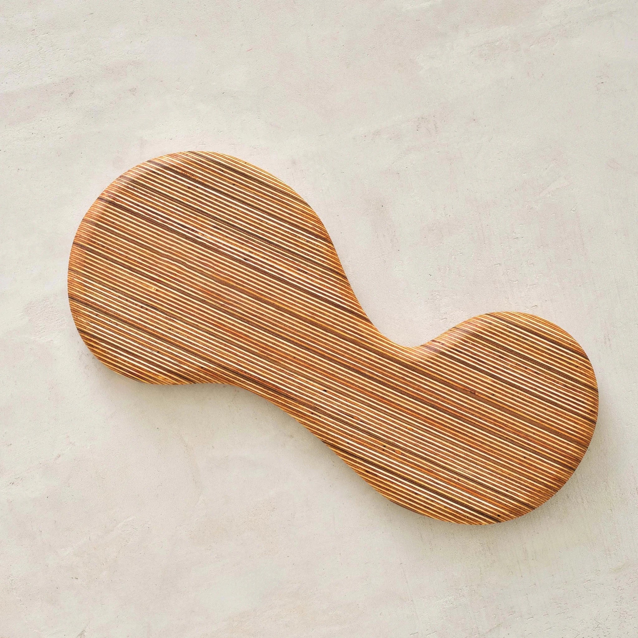 Peanut-shaped layered Baltic birch valet tray with striped edge grain on pale plaster