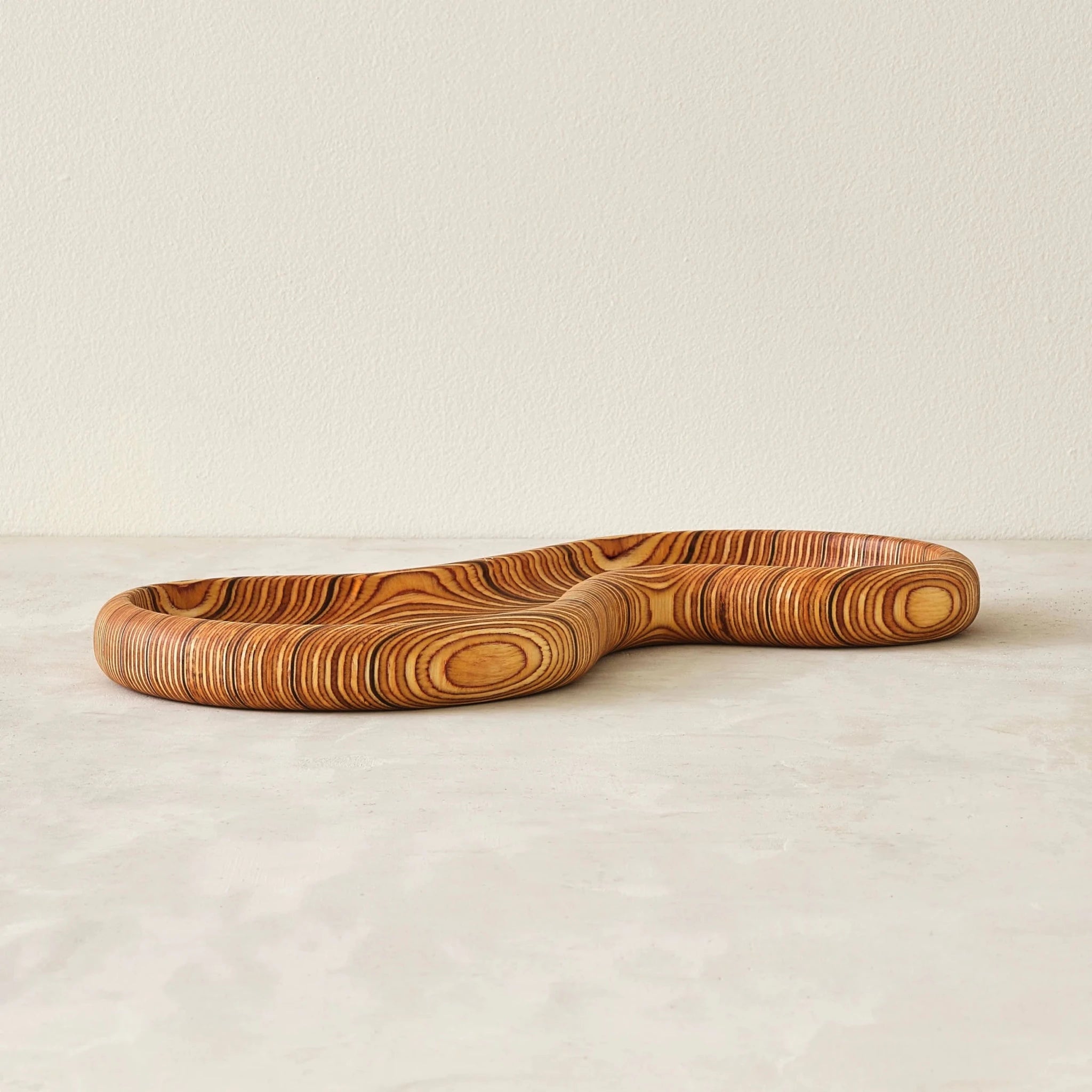 Curved wooden tray side view showing concentric layered birch grain, neutral background
