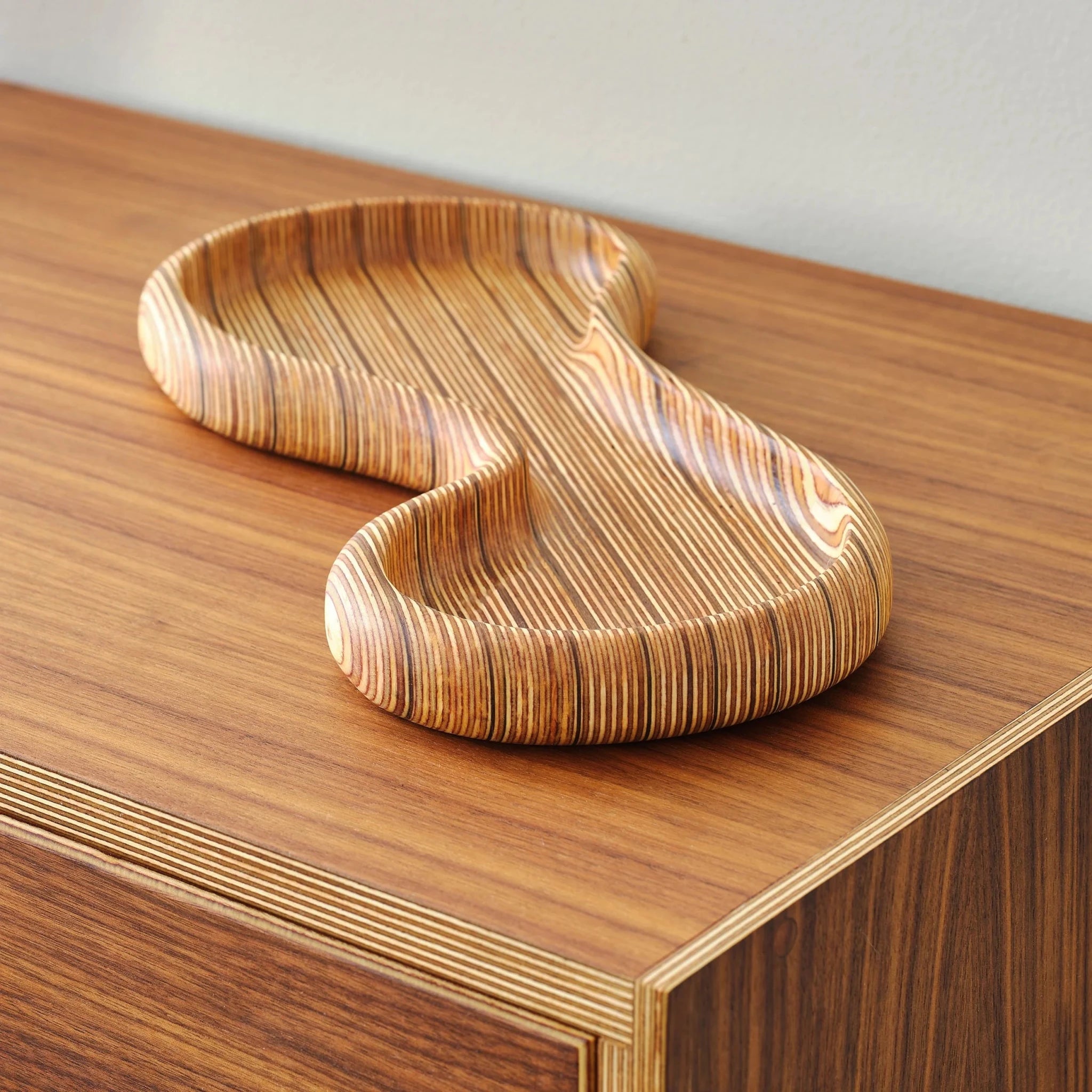 Curved birch plywood tray with concentric grain resting on walnut dresser top